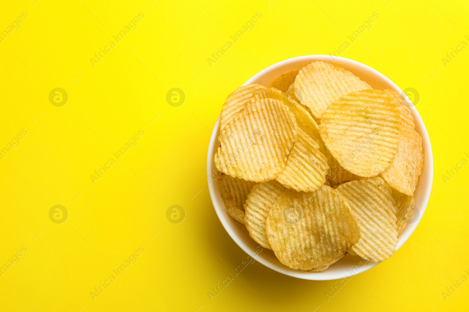 Photo of Delicious crispy potato chips in bowl on color background, top view with space for text