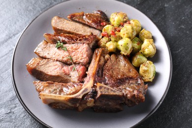 Photo of Delicious fried beef meat, vegetables and thyme on black table, closeup