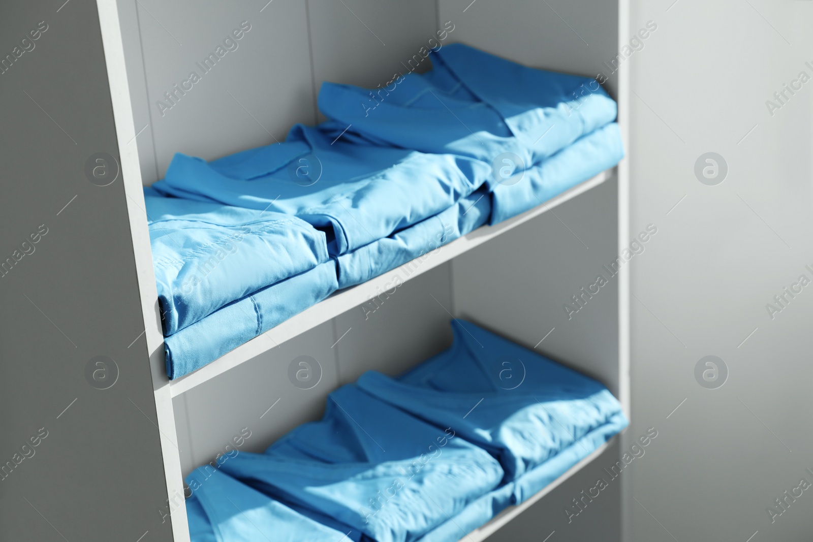 Photo of Light blue medical uniforms on white rack indoors