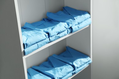 Photo of Light blue medical uniforms on white rack indoors