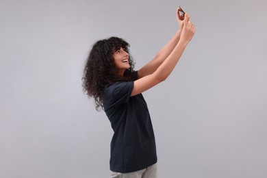 Beautiful young woman taking selfie on light grey background