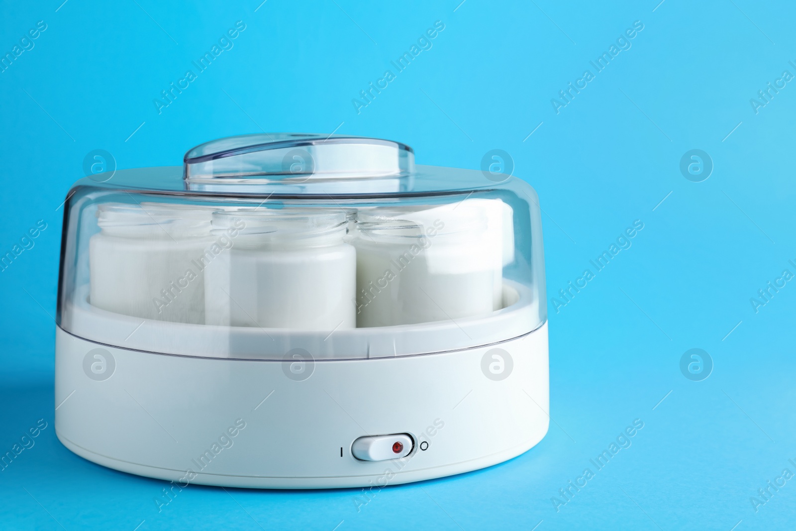 Photo of Modern yogurt maker with full jars on light blue background