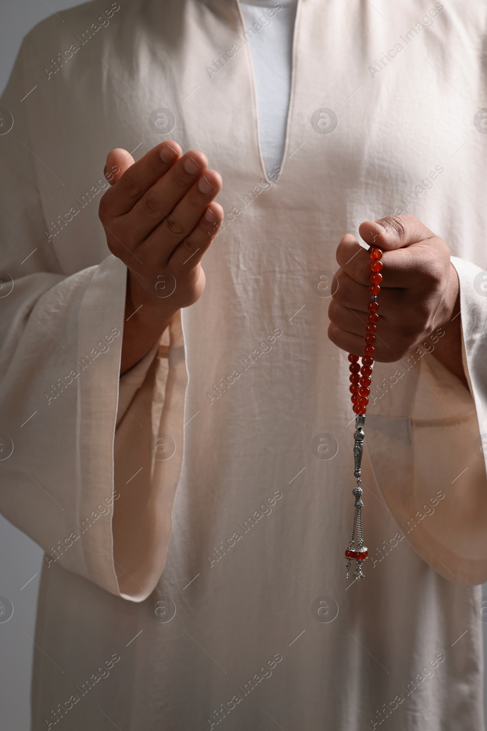 Photo of Muslim man with misbaha praying on light grey background, closeup