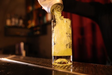 Photo of Bartender pouring energy drink into glass at counter in bar, selective focus