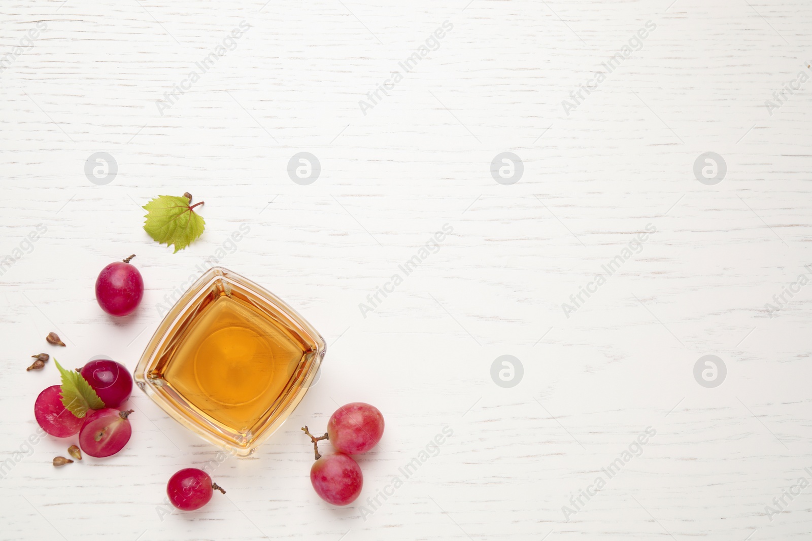 Photo of Flat lay composition with bowl of natural grape seed oil on white wooden table, space for text. Organic cosmetic