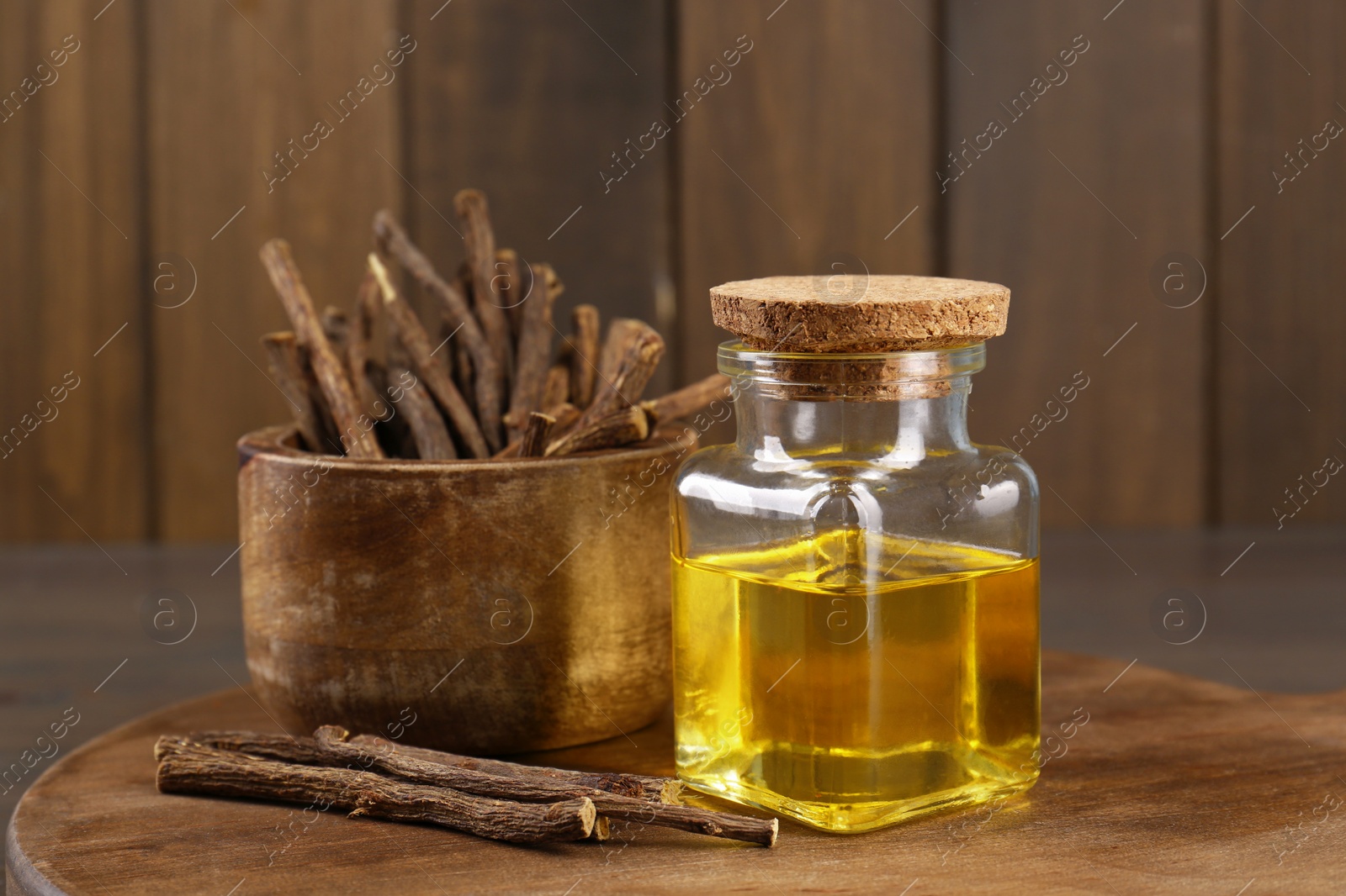 Photo of Dried sticks of licorice roots and essential oil on wooden board, closeup