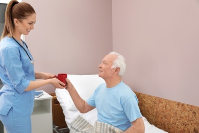 Nurse giving drink to senior man in hospital ward. Medical assisting