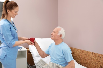 Photo of Nurse giving drink to senior man in hospital ward. Medical assisting