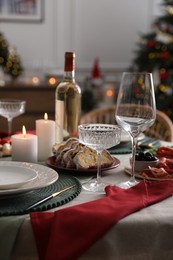 Photo of Christmas table setting with burning candles, appetizers and dishware indoors