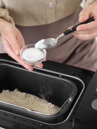 Photo of Making dough. Woman adding salt into breadmaker machine, closeup