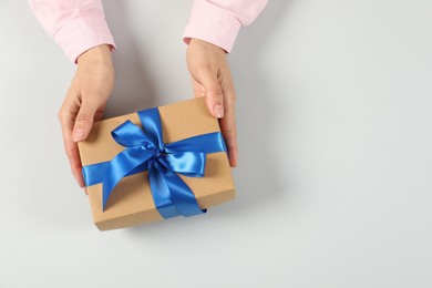 Photo of Woman holding gift box on light background, top view. Space for text