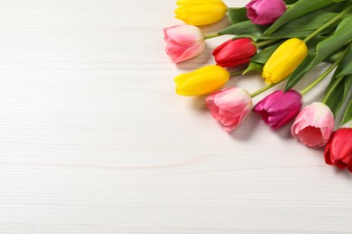 Photo of Beautiful colorful tulips on white wooden table, above view. Space for text