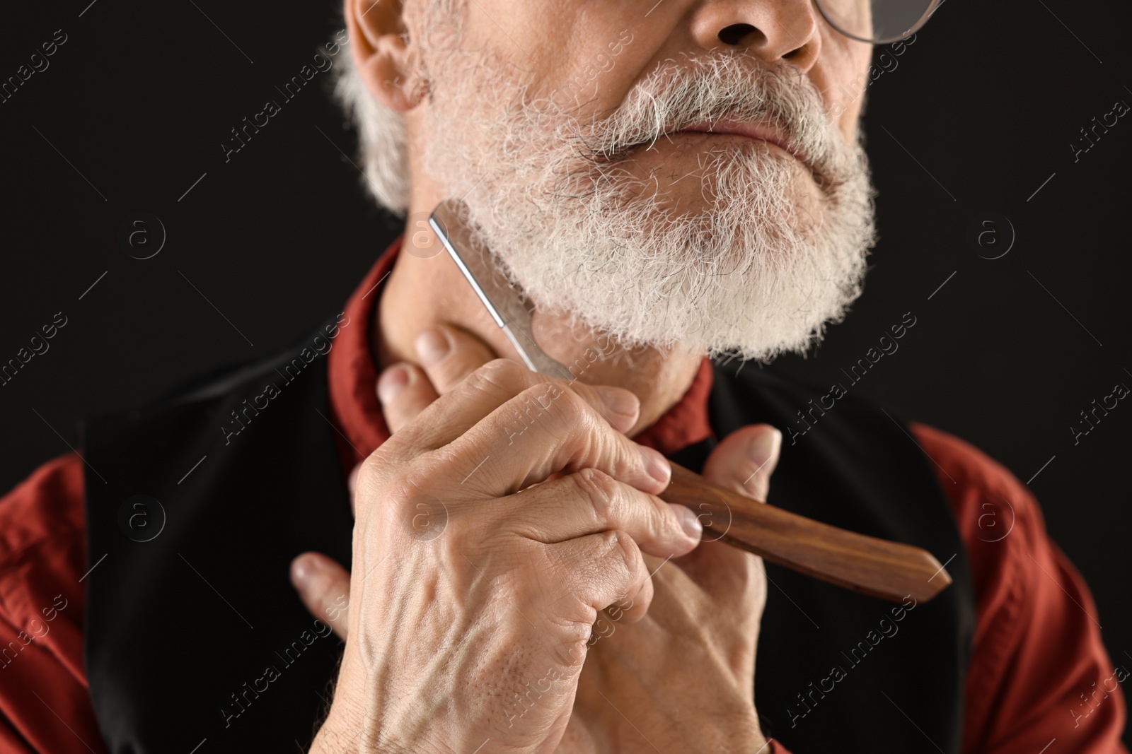 Photo of Man shaving beard with blade on black background, closeup