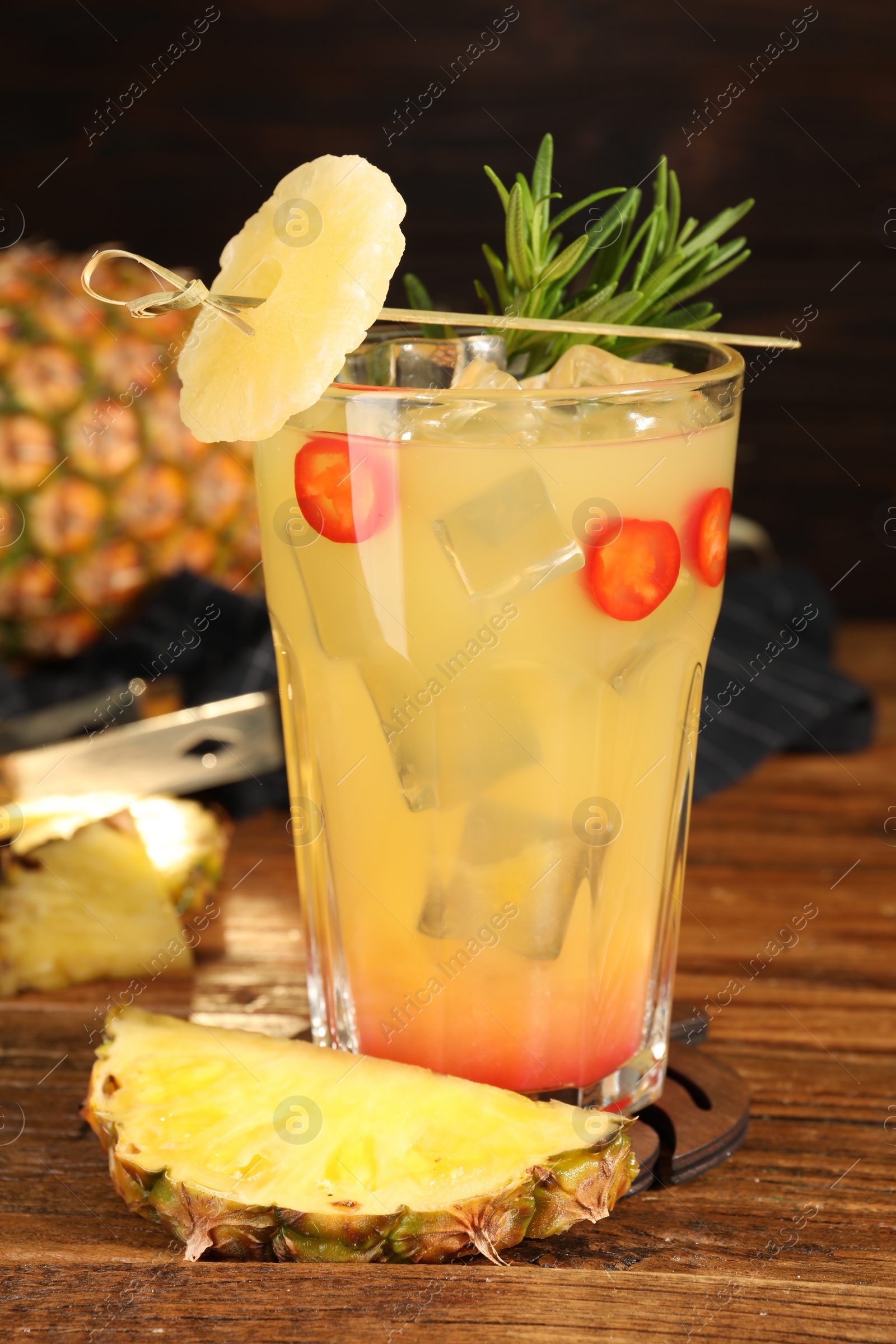 Photo of Spicy pineapple cocktail with chili pepper, rosemary and fresh fruit on wooden table