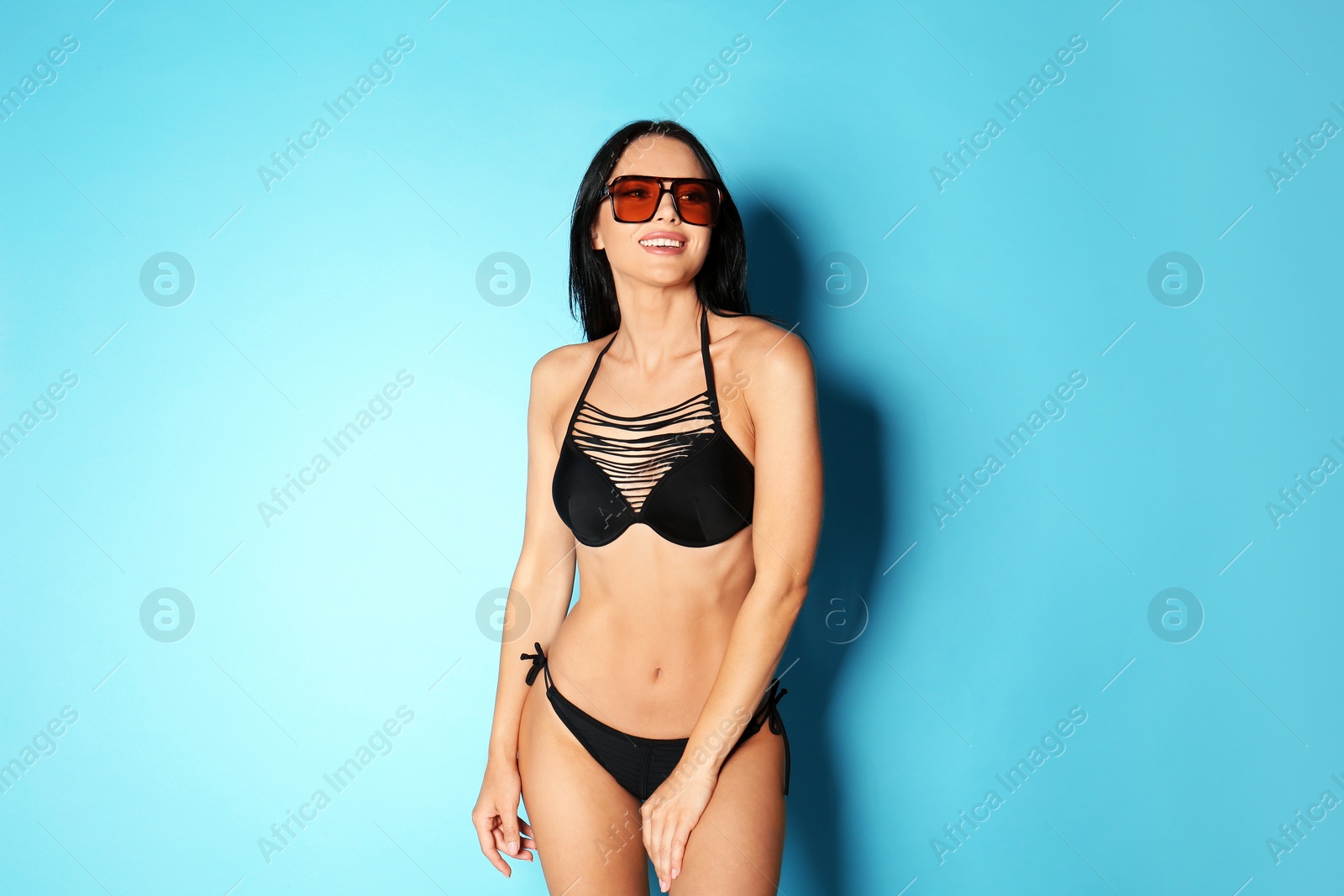 Photo of Beautiful young woman in black bikini with sunglasses on light blue background