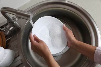 Photo of Woman washing plate in kitchen sink, above view