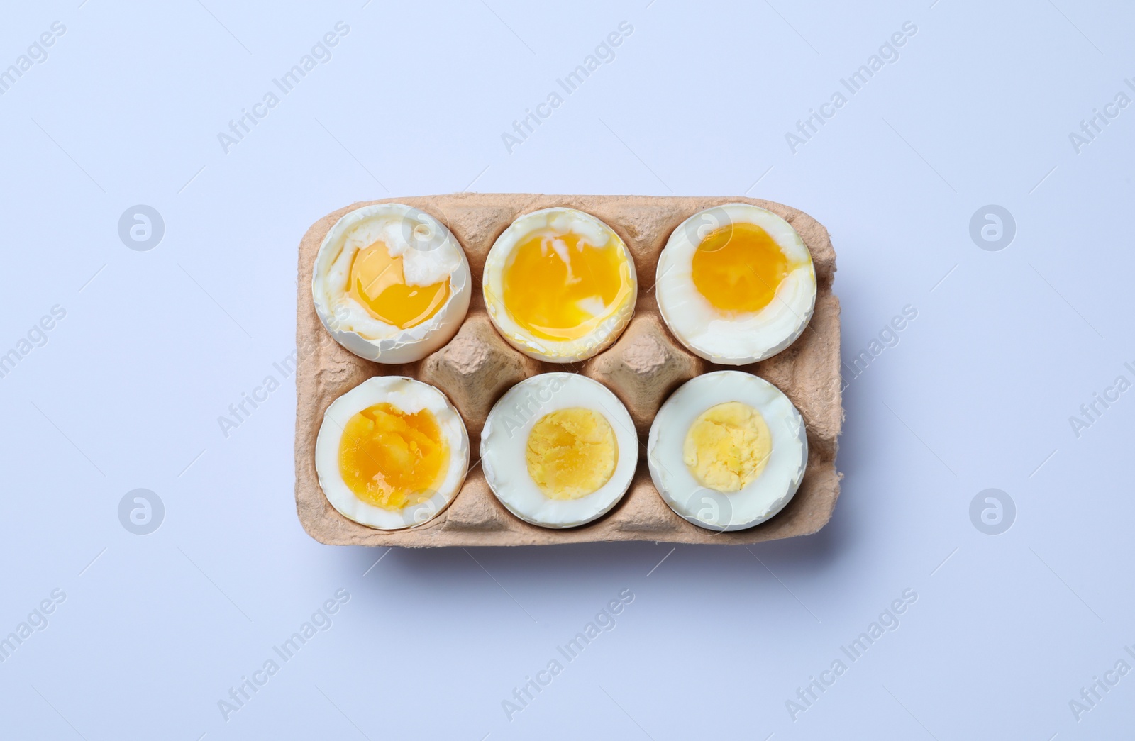 Photo of Boiled chicken eggs of different readiness stages in carton on white background, top view