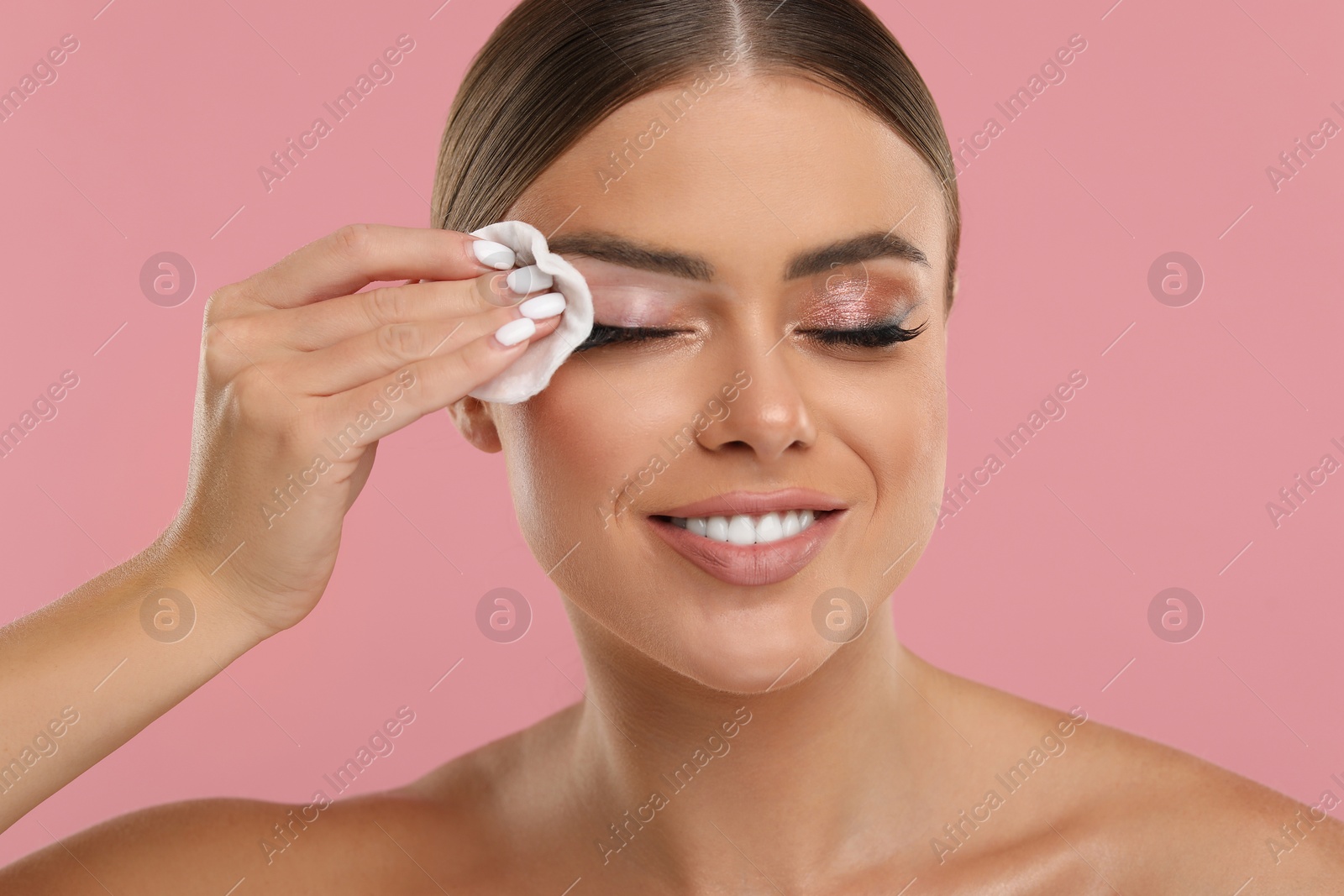 Photo of Beautiful woman removing makeup with cotton pad on pink background