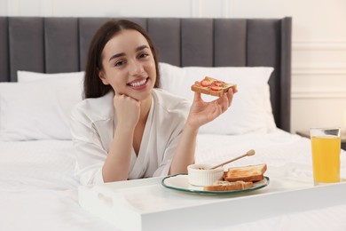 Happy young woman having breakfast on bed at home