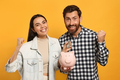 Happy couple with ceramic piggy bank and money on orange background