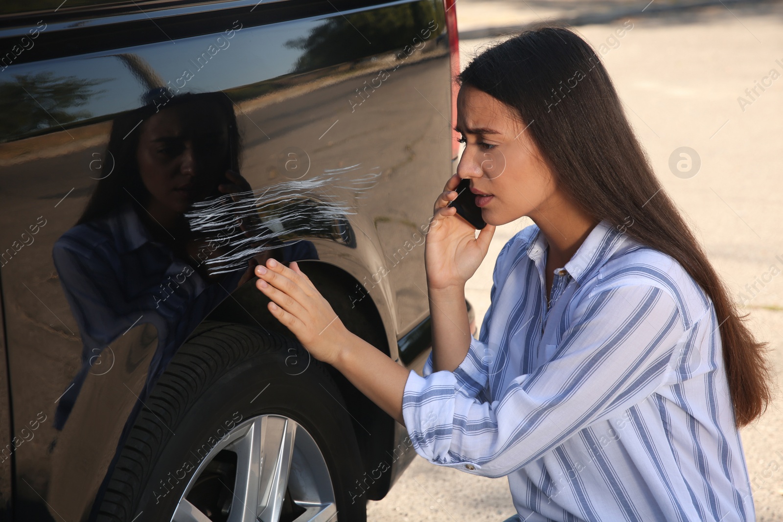 Photo of Stressed woman talking on phone near car with scratch outdoors