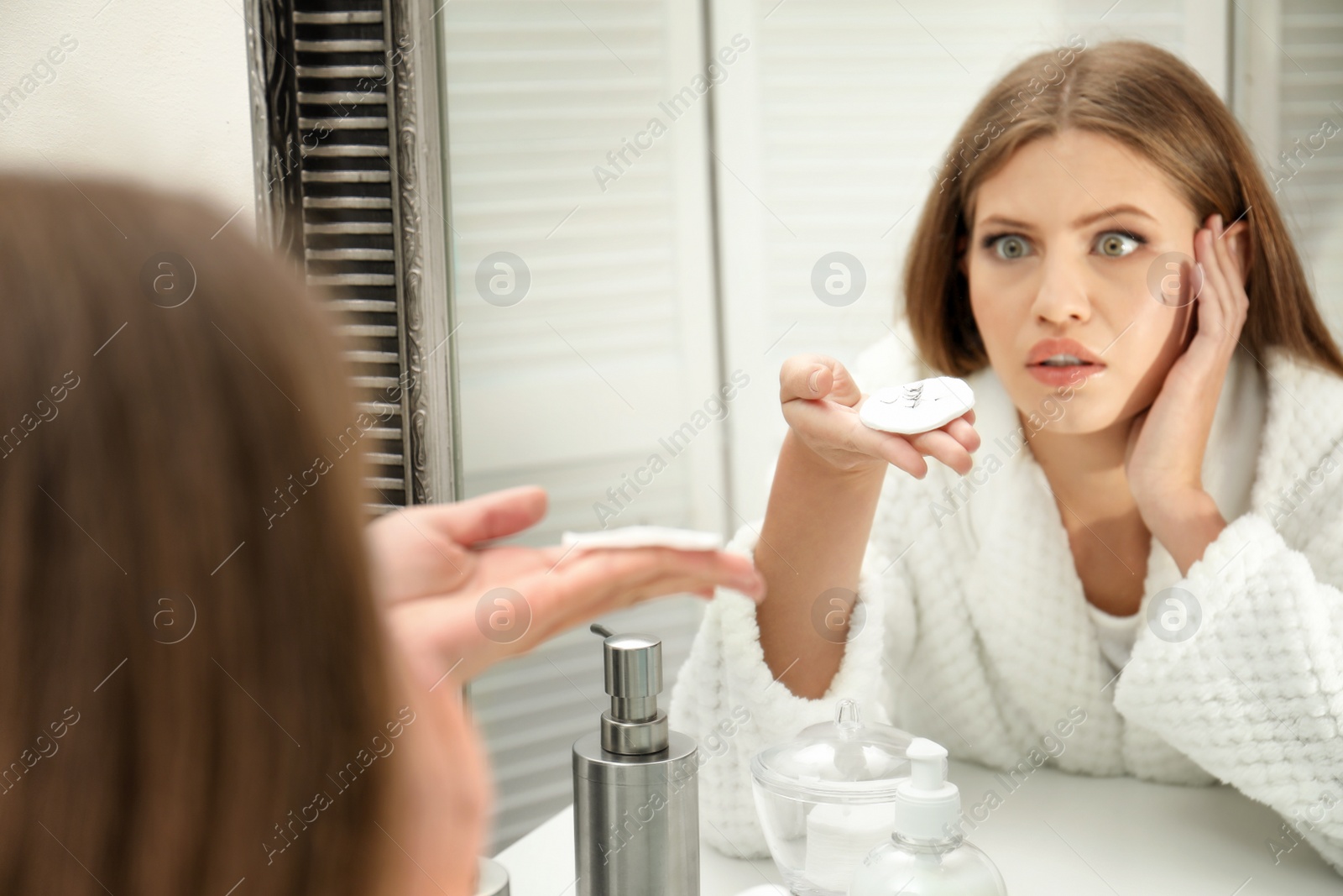 Photo of Emotional young woman with fallen eyelashes near mirror in bathroom