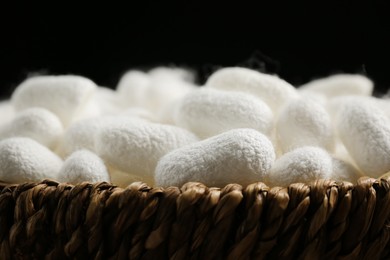 Photo of White silk cocoons in wicker bowl on black background, closeup