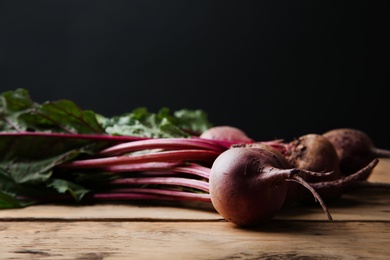 Bunch of fresh beets with leaves on wooden table against black background. Space for text