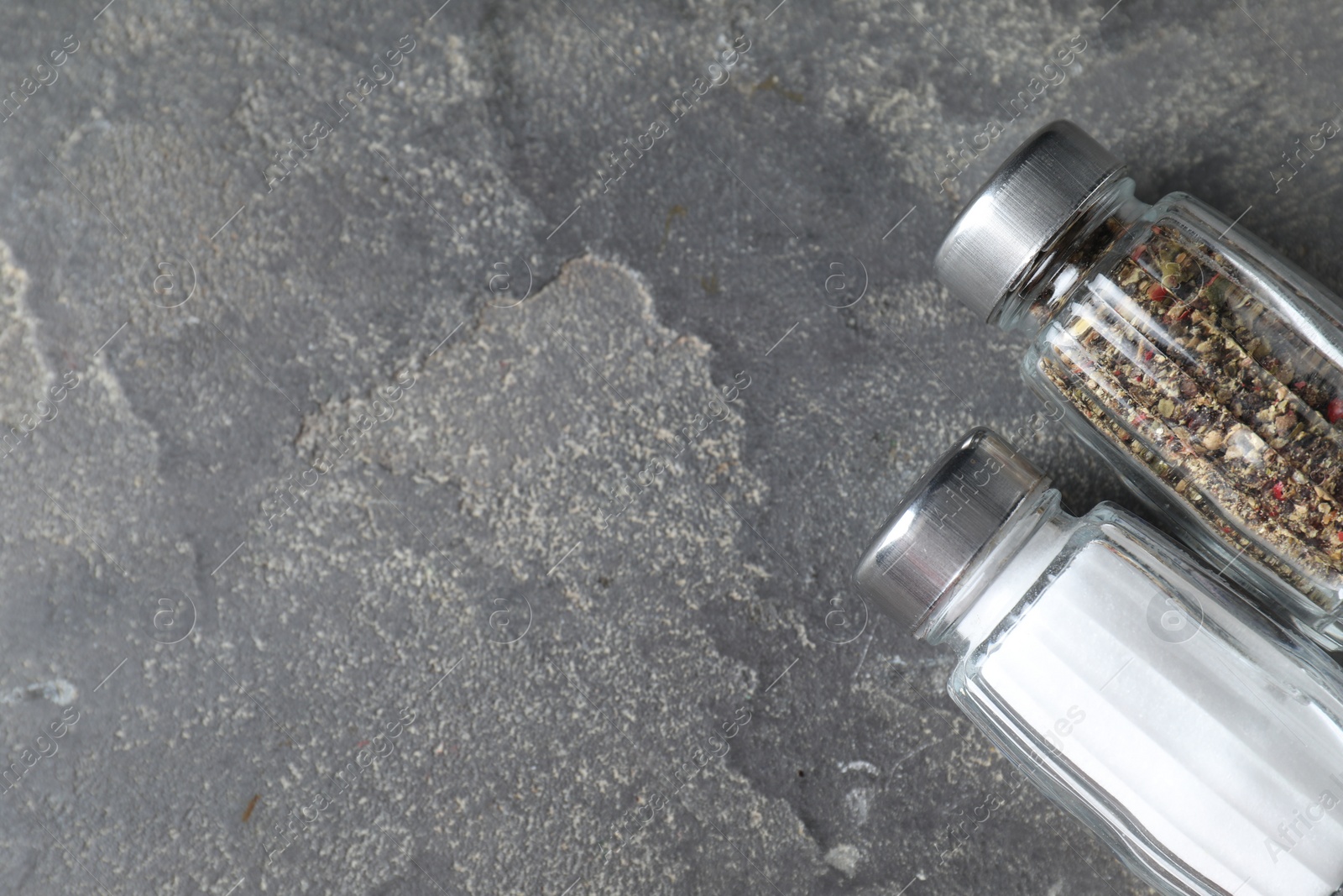 Photo of Salt and pepper shakers on grey textured table, top view. Space for text