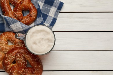 Tasty freshly baked pretzels and mug of beer on white wooden table, flat lay. Space for text