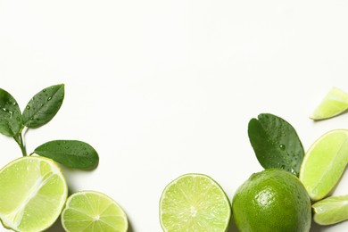 Whole and cut fresh ripe limes with green leaves on white background, flat lay