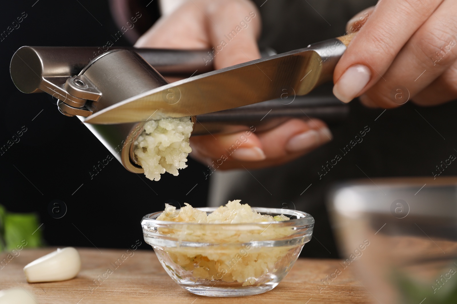 Photo of Woman squeezing garlic with press at wooden table, closeup