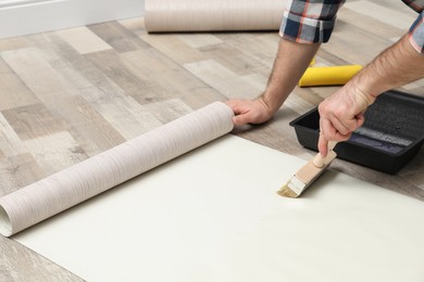 Photo of Man applying glue onto wall paper on floor, closeup