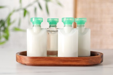 Mini bottles of cosmetic products on white table against blurred background