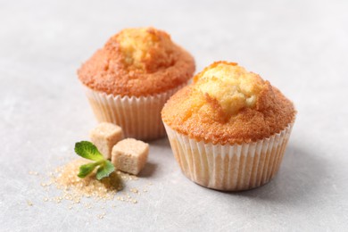 Delicious sweet muffins and brown sugar on light grey textured table, closeup