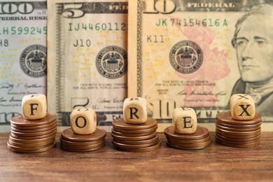 Photo of Word Forex made of wooden cubes with letters and stacked coins near banknotes on table