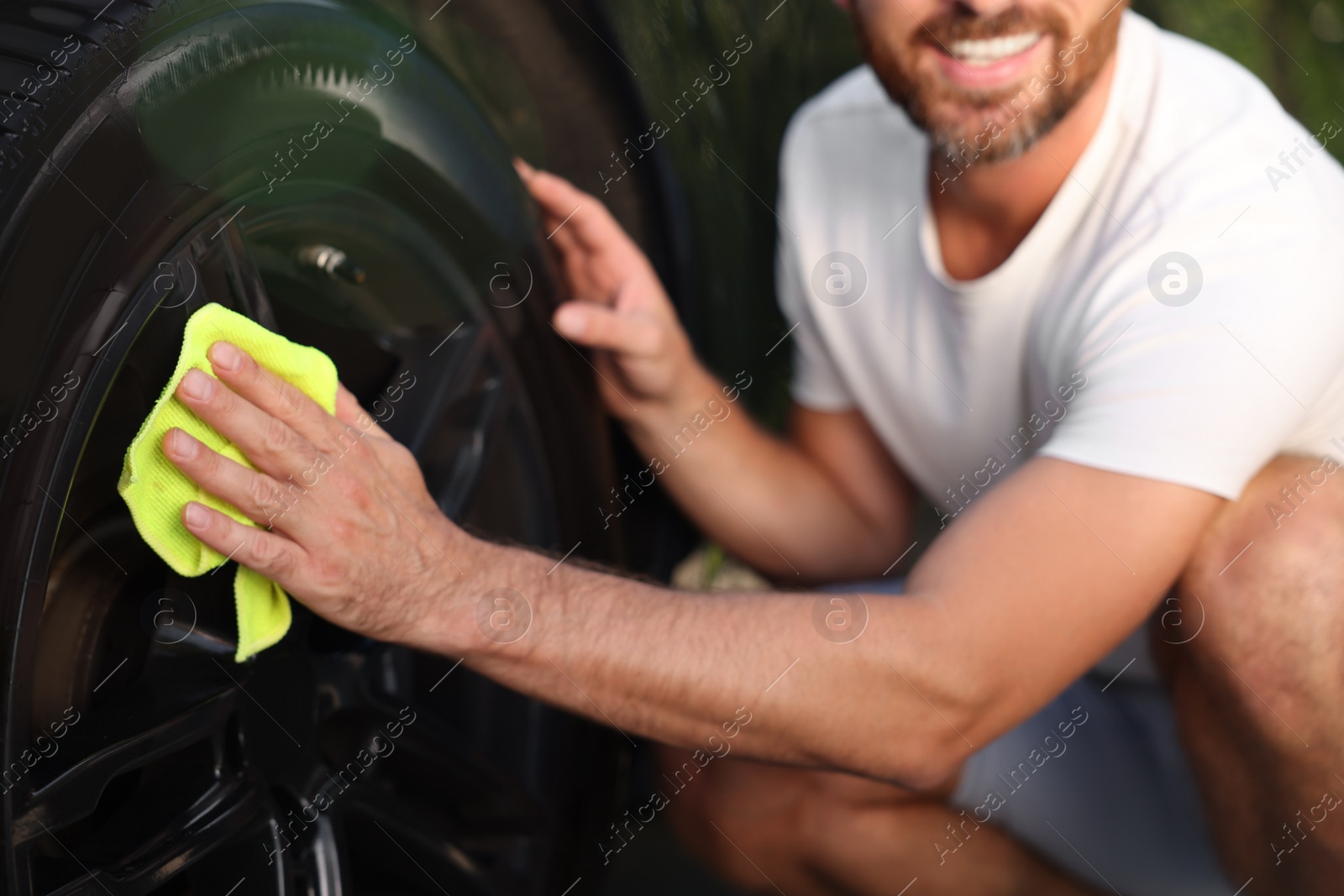 Photo of Man washing car wheel with rag outdoors, closeup
