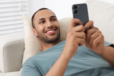 Happy man sending message via smartphone indoors