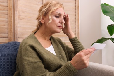 Photo of Upset middle aged woman with envelope on sofa at home. Loneliness concept