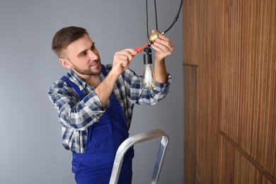 Electrician with screwdriver repairing ceiling lamp indoors. Space for text