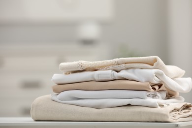 Photo of Stack of different folded clothes on white table indoors, closeup