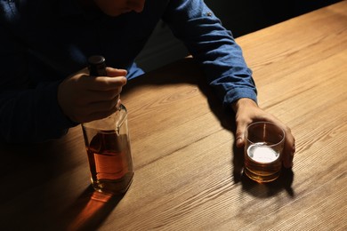 Photo of Addicted man with alcoholic drink at wooden table, closeup