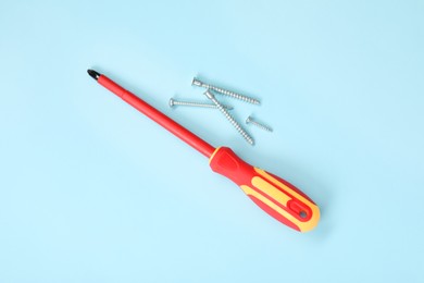 Photo of Screwdriver with red handle and screws on light blue background, flat lay