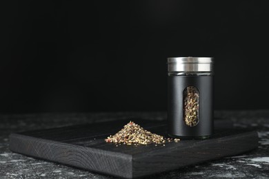 Stylish shaker with pepper on dark table against black background. Space for text
