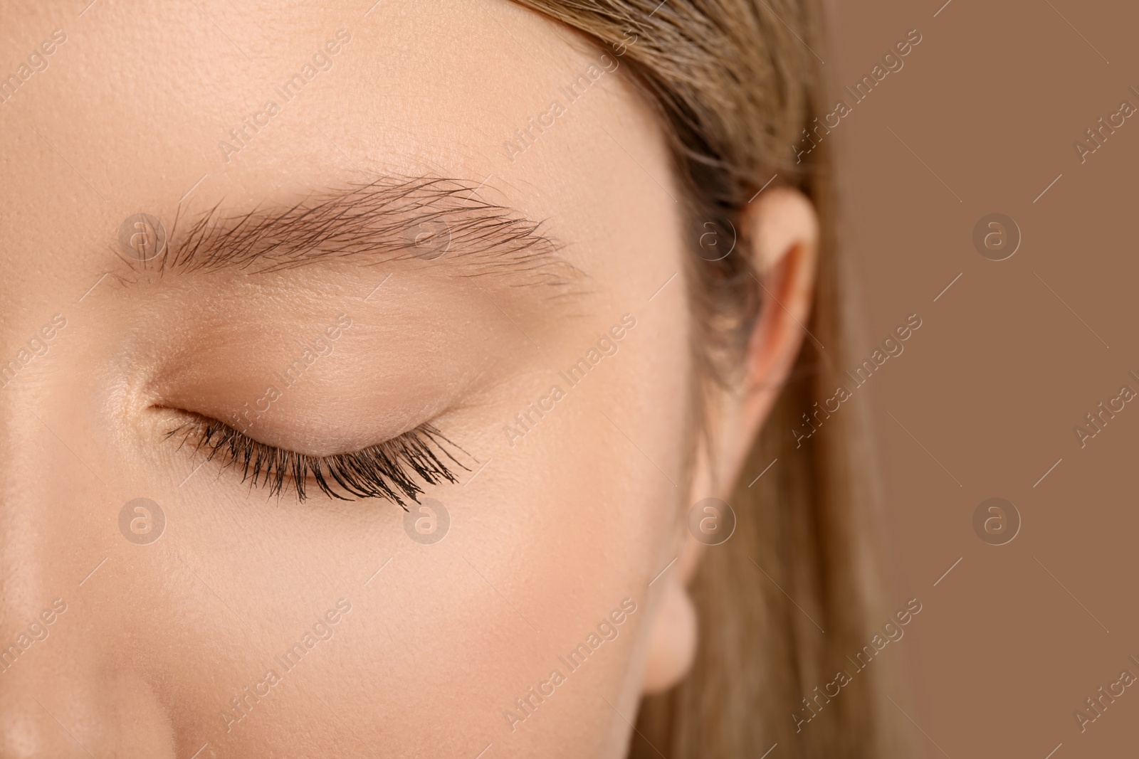 Photo of Woman with long eyelashes after mascara applying against light brown background, closeup