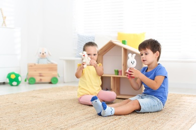 Photo of Cute little children playing with toys near wooden house on floor at home