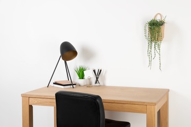 Comfortable workplace with wooden desk near white wall at home