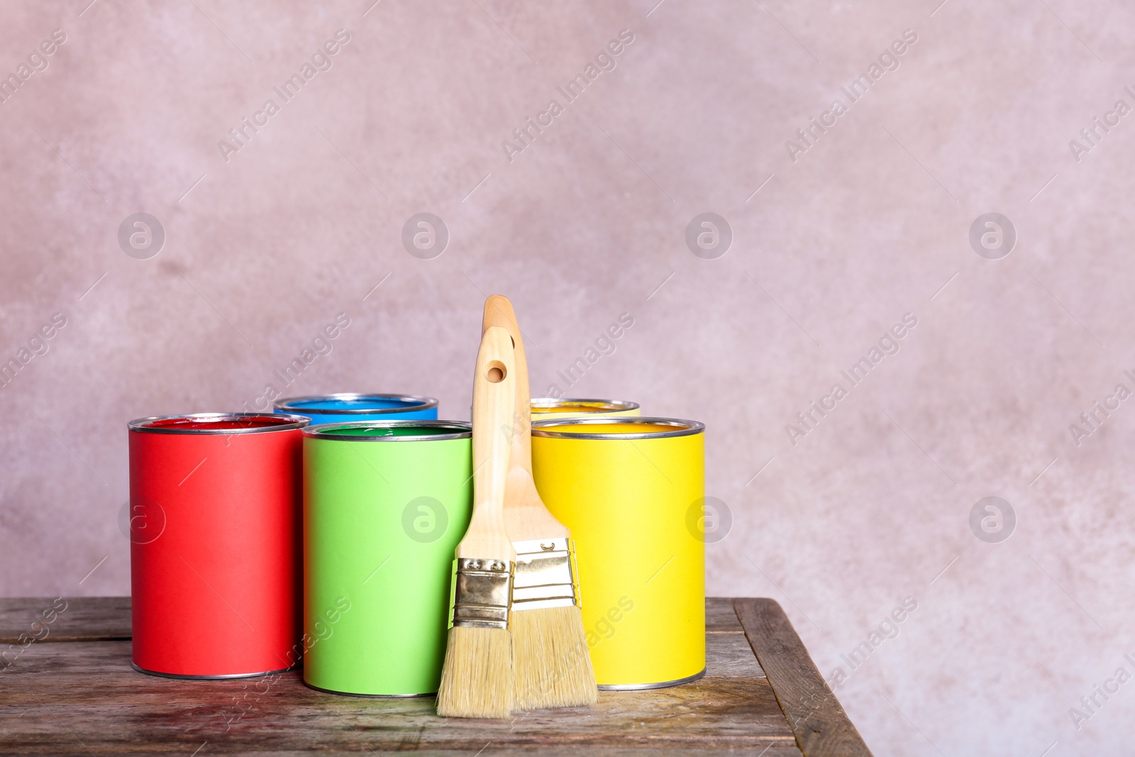Photo of Paint cans and brushes on table against color background. Space for text