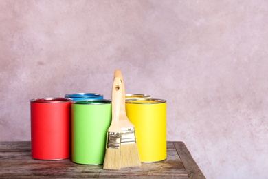 Paint cans and brushes on table against color background. Space for text