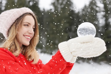 Young woman in winter clothes holding snow globe outdoors